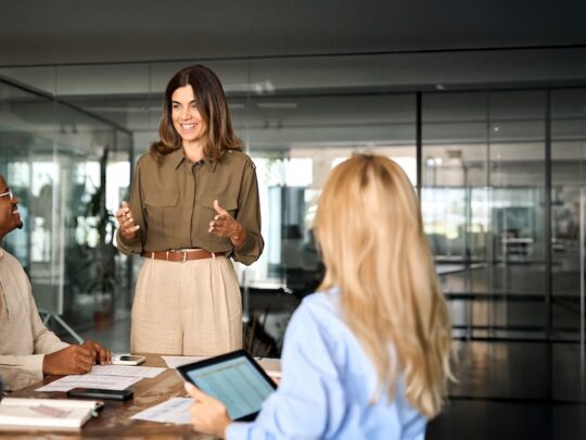 Happy middle aged business woman executive ceo leader discussing project management planning strategy working with diverse colleagues company team at office corporate board group meeting.